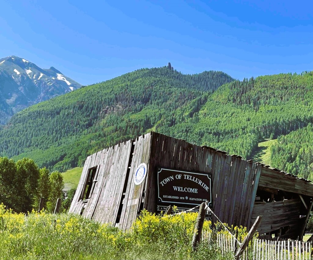 Welcome to Telluride sign with a crumbling building and wild flowers